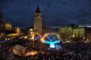 Otoczona przez tłumną widownię rozświetlona scena nocą ustawiona na krakowskim Rynku Głównym. Na przodzie sceny ktoś stoi. Scena jest półokrągła z wybiegiem w kierunku publiczności. Za sceną Wieżą Ratuszowa i zabudowania, po lewej stronie Sukiennice, po prawej kamienice oraz ogródki kawiarniane. Między publicznością wydzielony jest pusty teren z zadaszoną wiatą – jest to miejsce dla ekipy telewizyjnej.
